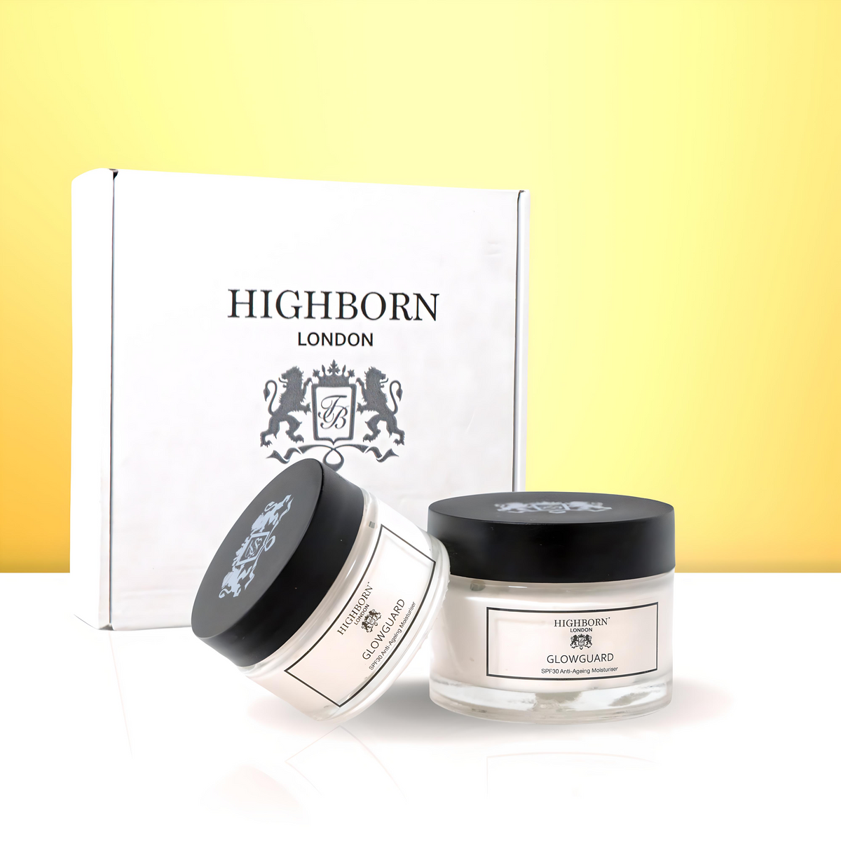 Two Highborn London GLOWGUARD SPF30 Anti-Ageing Moisturiser jars (one upright, one angled) in front of the white branded outer gift box on a yellow background